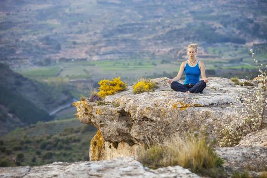 Young woman sitting on a rock and enjoying valley view. Girl sits in asana position.