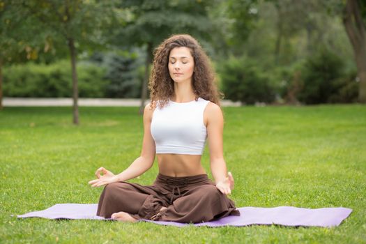 Pretty woman doing yoga exercises in outdoor park, green grass background 