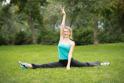 Beautiful young woman doing stretching exercises in the park. Green grass  background 