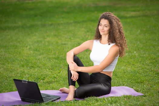 Portrait of sporty young businesswoman sitting with laptop. Green grass background 