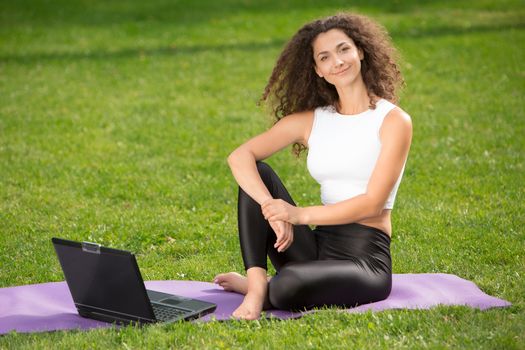 Portrait of sporty young businesswoman sitting with laptop. Green grass background 