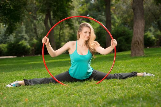 Young female athlete sitting in the splits inside hula hoop in the park. Green grass backgruond