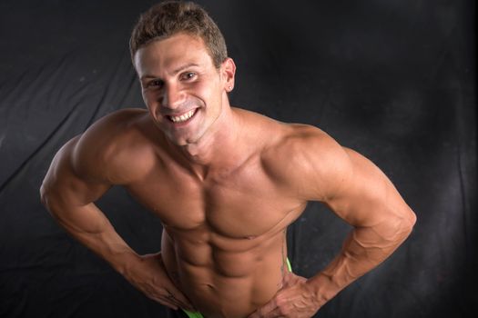 Handsome shirtless bodybuilder shot from above, standing on dark background wearing trunks