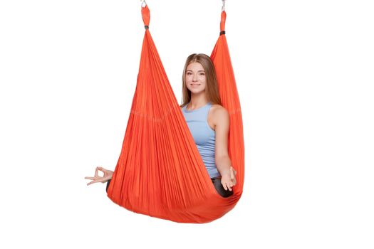 Young woman doing anti-gravity aerial yoga in red hammock on a seamless white background.