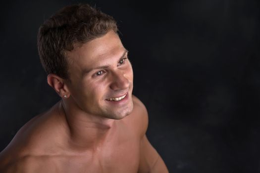 Head and shoulder shot of shirtless handsome young man smiling, on dark background