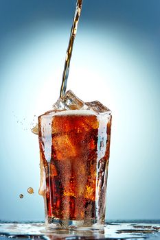 Cola pouring in a glass  with ice on a blue background
