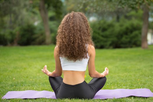 Pretty woman sitting back doing yoga meditation in the lotus position. Green grass background 