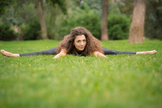 Beautiful young woman doing stretching exercises in the park. Green grass  background 