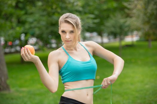 Sporty young woman with apple and measuring tape. Outdoors. Concept of healthy lifestyle.
