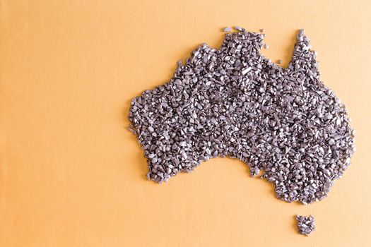 Conceptual map of Australia formed of small silvery stones on a yellow textile background with weave detail and copyspace