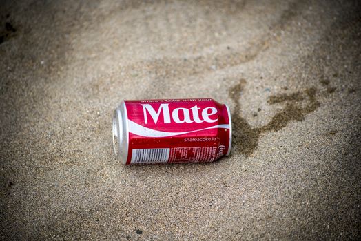 coca cola can washed up on sandy beach with the name mate printed on it