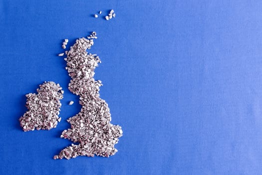 Conceptual map of the United Kingdom and Republic of Ireland formed of decorative silvery stones over a blue textile background with copyspace and weave detail