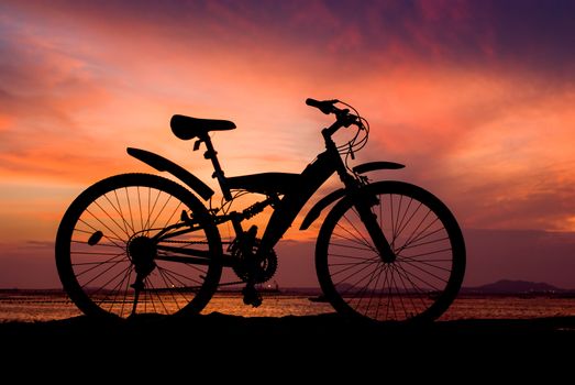 Silhouette of mountain bike parking on jetty beside sea with sunset sky background