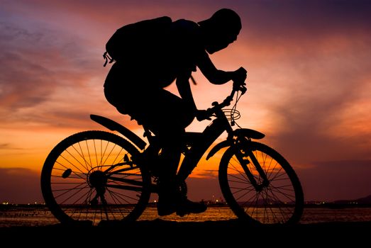 Silhouette of backpacker ride mountain bike on bridge beside sea with sunset sky background