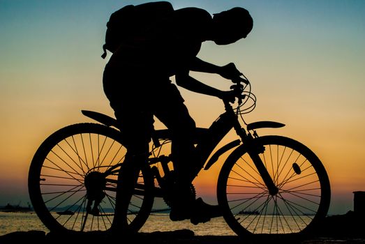 Silhouette of backpacker ride mountain bike on bridge beside sea with sunset sky background