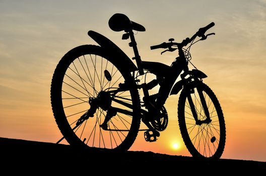 Silhouette of mountain bike parking on jetty beside sea with sunset sky background