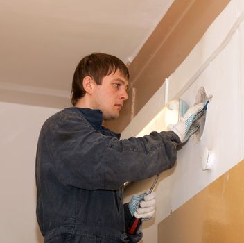 
Electrician repairing wiring hidden in the wall of a building under plaster
