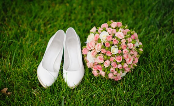 wedding bouquet and shoes lying down on green grass.