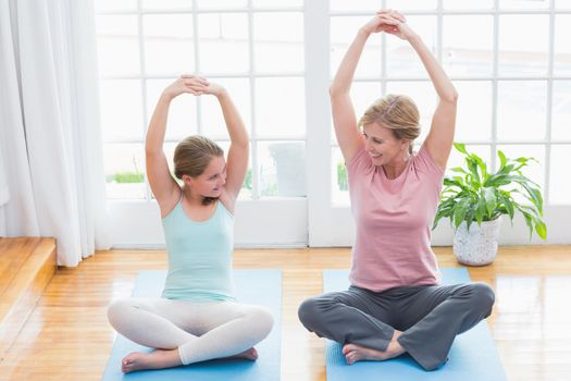 Mother and daughter doing yoga on fitness mat at home in living room 