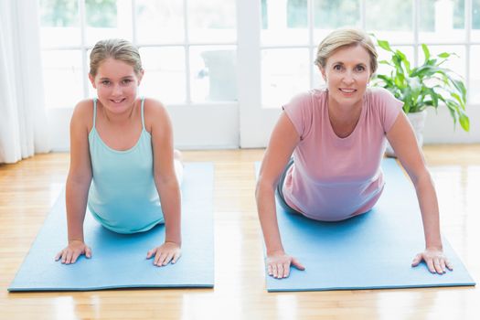 Happy mother and daughter doing yoga at home in the living room 