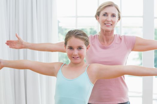 Happy mother and daughter doing yoga at home in the living room 