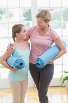 Mother and daughter holding yoga mats at home in the living room 