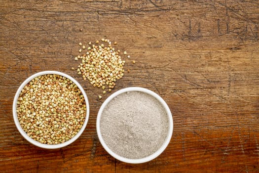 gluten free buckwheat grain and flour - top view of two ceramic bowls against rustic wood with a copy space