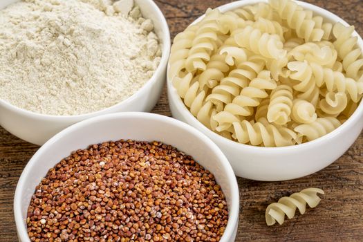 gluten free quinoa grain, flour and pasta on small ceramic bowls - healthy eating concept