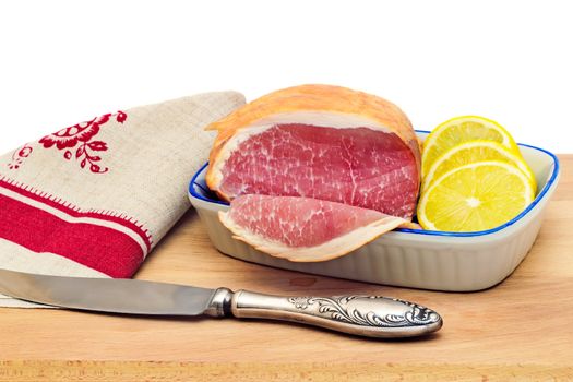 On a cutting Board is ham, bread, lemon and tomato. Presented on a white background.