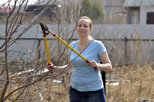 The woman in a garden cuts off branches secateurs with long handles in the spring