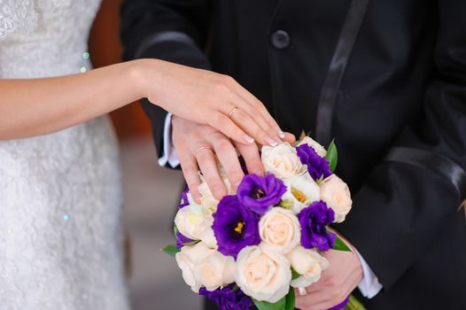 Hands of the groom and the bride on wedding bouquet