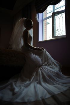 Young beautiful bride waits for groom near the window