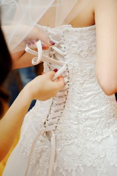 Bridesmaid is helping the bride to dress