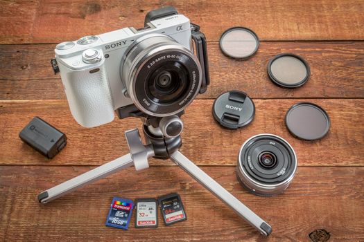 FORT COLLINS, CO, USA, April 17,  2015:  Sony A6000 mirrorless digital camera on a table tripod surrounded by a set of filters, memory cards, lens cap, battery and lens  on a grunge barn wood table.