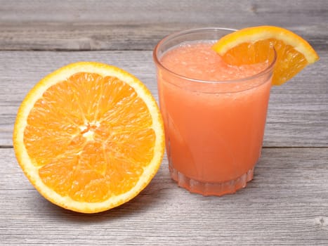 Glass of orange juice with sliced orange half on wooden table
