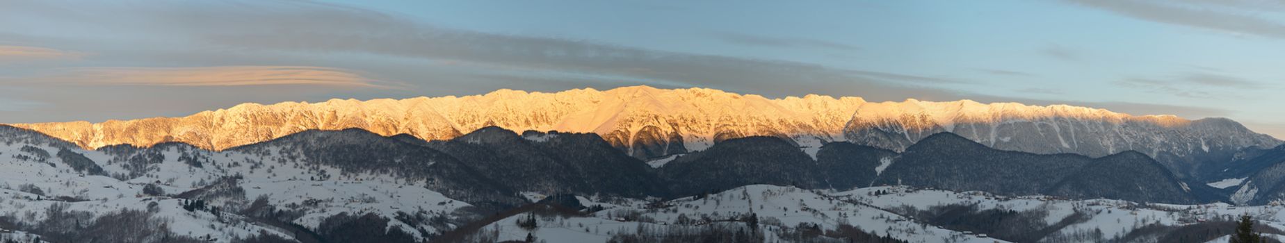 Alpine landscape with peaks covered by snow and clouds, view to Piatra Craiului mountains. Panorama view at sunrise.