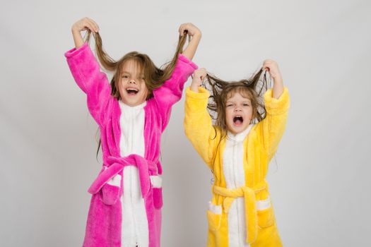Two sister girls with wet hair standing in the bath robes on a light background