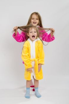 Two sister girls with wet hair standing in the bath robes on a light background