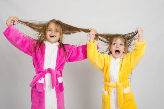 Two sister girls with wet hair standing in the bath robes on a light background