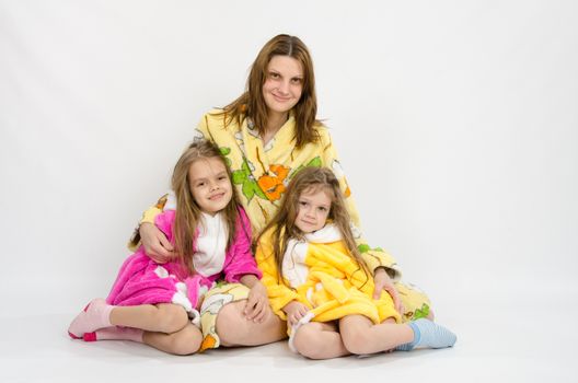 Mom with two daughters sitting in the bath robes on a white background