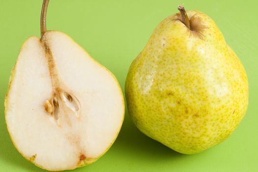 green pear cut in half on a green floor and a whole pear