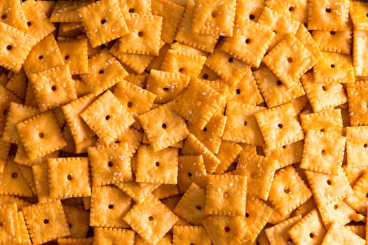 Background texture of square cheese crackers with central holes arranged in a layer viewed close up full frame from above