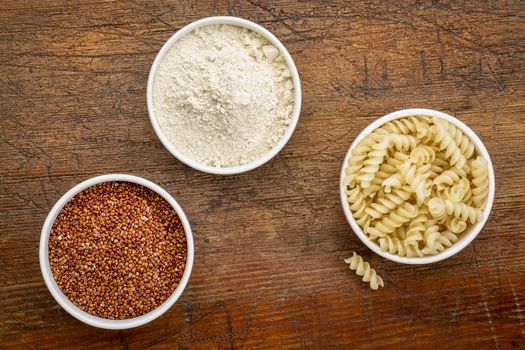 gluten free quinoa grain, flour and pasta - top view of small ceramic bowls against rustic wood