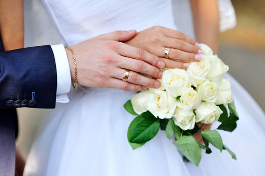 hands of the bride and groom on a white wedding bouquet
