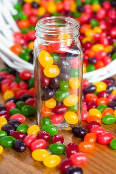 Jelly beans in a glass jar with a spilled basket of jelly beans behind it.