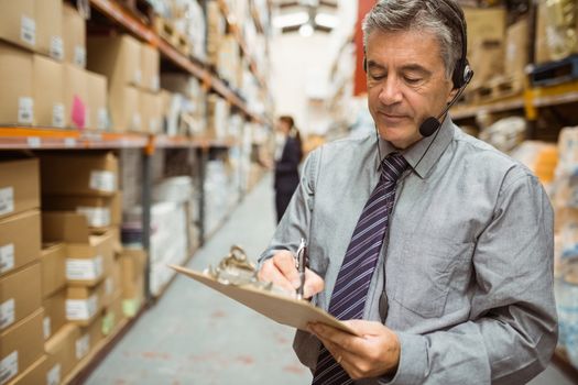 Warehouse manager writing on clipboard in a large warehouse