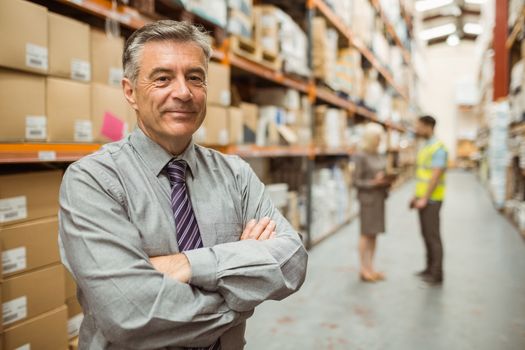 Smiling businessman with crossed arms in a large warehouse