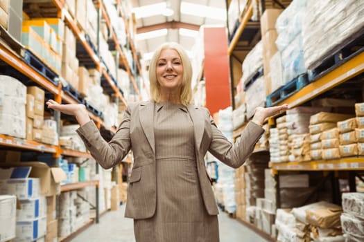 Smiling female manager showing with her hands in a large warehouse