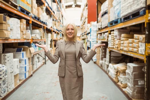 Smiling female manager showing with her hands in a large warehouse