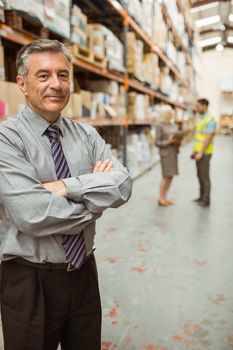 Smiling businessman with crossed arms in a large warehouse